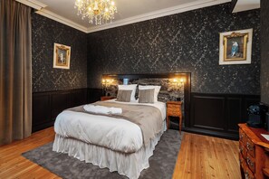 Quarto com cama grande, paredes escuras texturizadas, lustre e quadros emoldurados.
