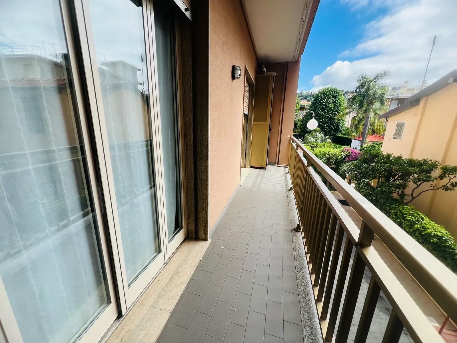 A balcony with a tiled floor, a metal railing, and a view of greenery and buildings in the distance.