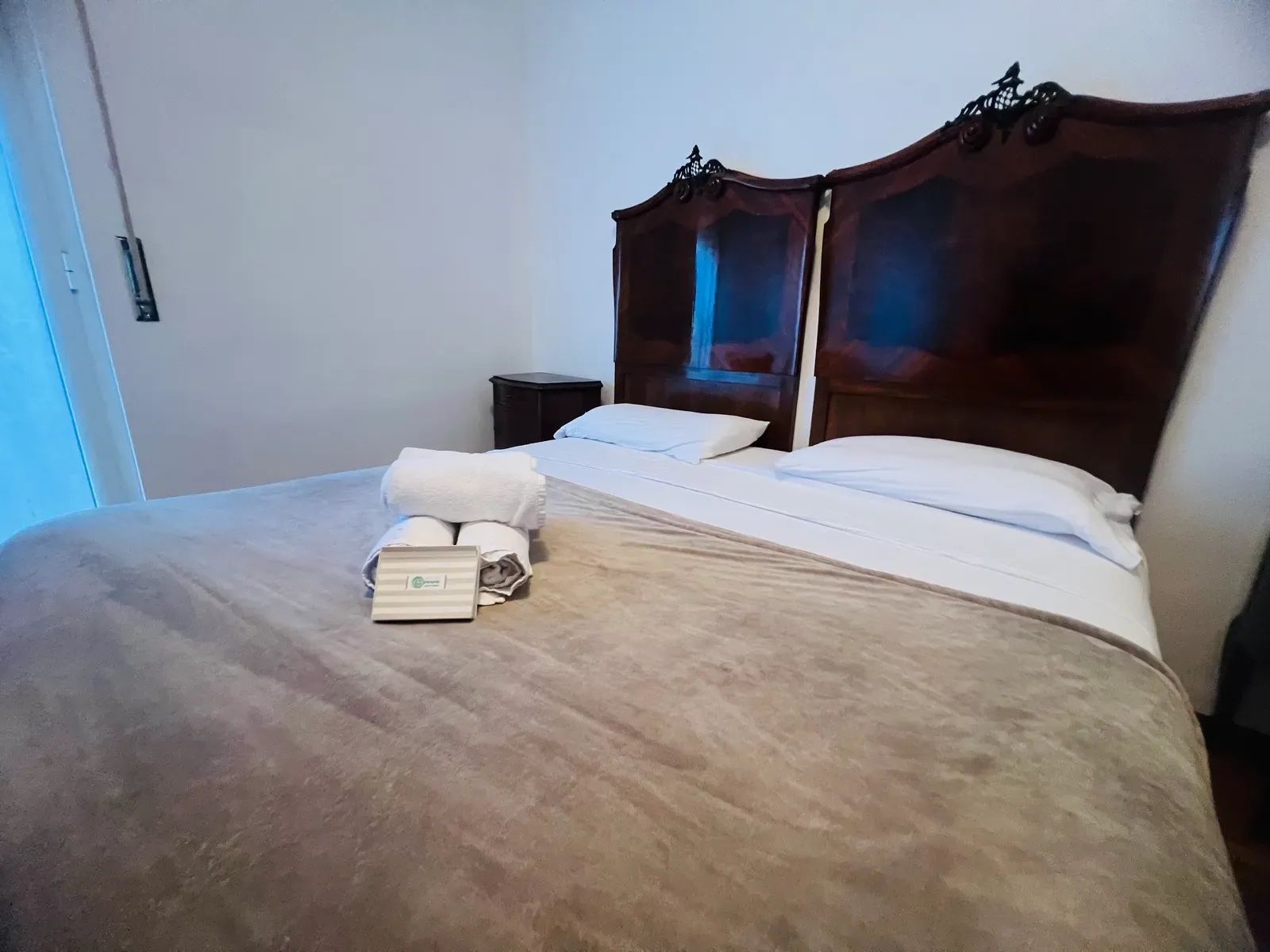 A hotel room with a large bed, two pillows, a bedside table, and a nightstand.