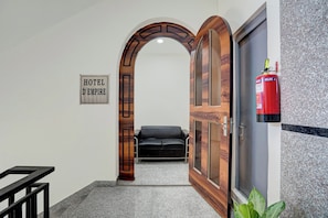 A hotel lobby with a sign reading 'HOTEL D'EMPIRE,' a black leather sofa, a wooden door, and a fire extinguisher. - Hotel O D'Empire (Gurugram)
