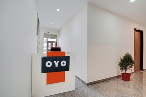 A reception desk with a sign that reads 'OYO' in a modern lobby with a potted plant and a door. - Hotel O D'Empire (Gurugram)