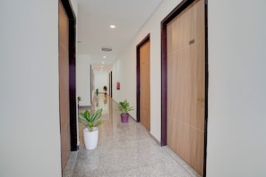 A hallway with wooden doors, potted plants, and a fire extinguisher. - Hotel O D'Empire (Gurugram)
