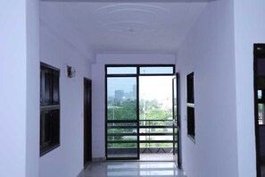 A corridor with a large sliding glass door leading to an outdoor balcony with a city view. - Hotel O the Front Door (Gurugram)