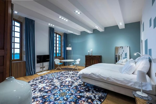 A bedroom with a bed, a desk, a chair, a large vase, and a patterned rug.