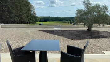 An outdoor seating area with a table and chairs, a gravel ground, and a view of a forest and fields.