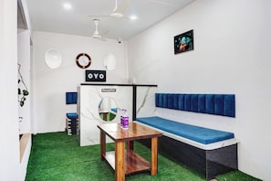 Zona de recepción con mostrador, un banco acolchado azul, ventilador de techo y un cartel en la pared.