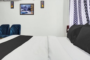 Una habitación de hotel con una cama, dos sillones, un cuadro en la pared y cortinas estampadas.