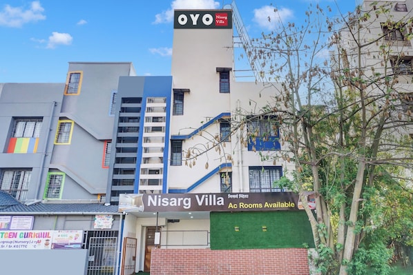 Un edificio con un letrero que indica 'Nisarg Villa', mostrando habitaciones con aire acondicionado disponibles.