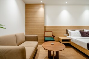 Ein modernes Hotelzimmer mit einer Couch, einem Sessel, einem kleinen Tisch, einem Bett und einem Nachttisch.