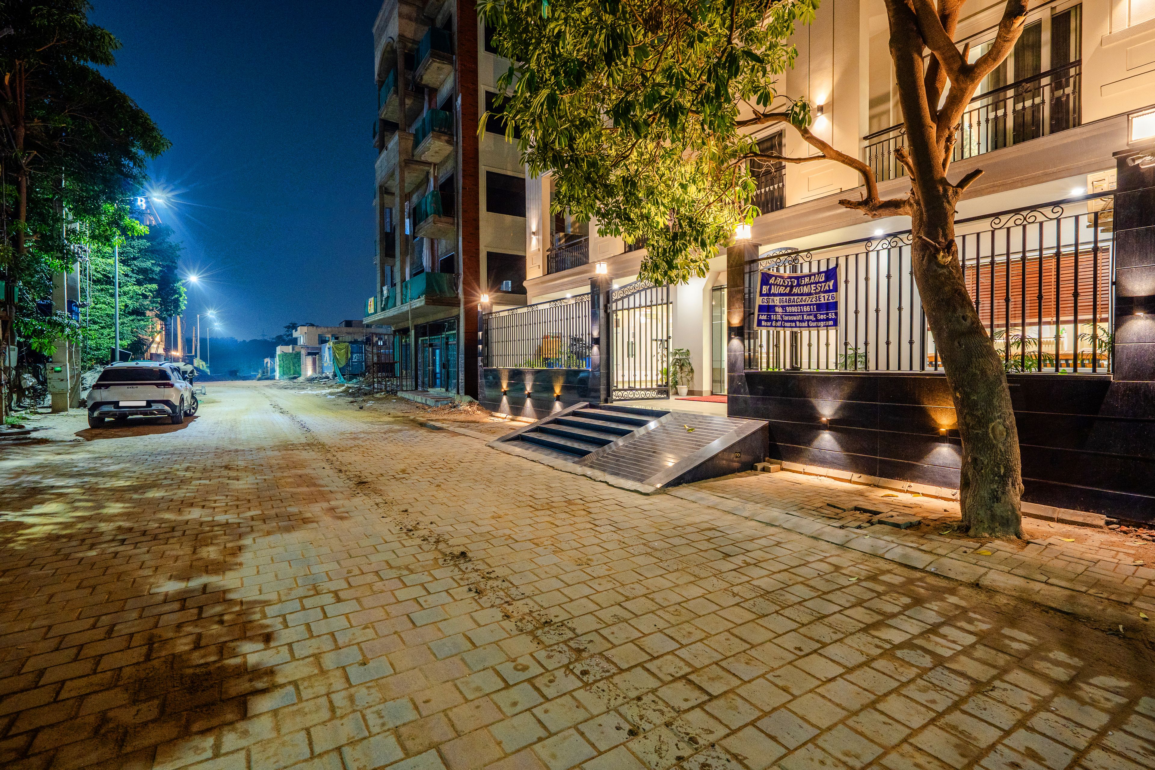 A nighttime street view with a building featuring a gated entrance, a staircase, and a parked car.