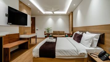 Quarto de hotel moderno com cama, mesa de cabeceira, escrivaninha, cadeira, televisão e ventilador de teto.