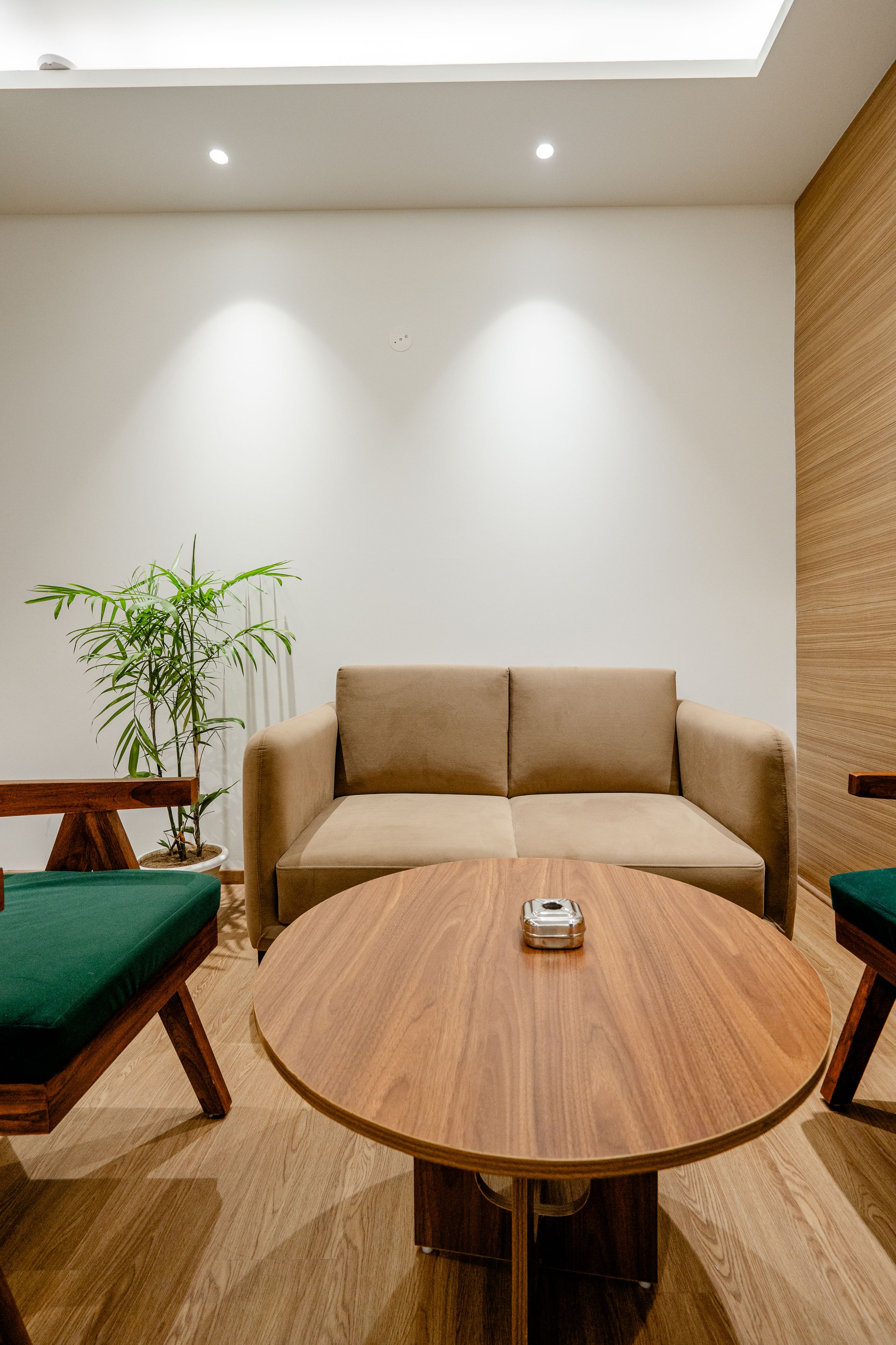 Uma sala de estar moderna com uma mesa de madeira redonda, um sofá bege e um banco estofado verde.