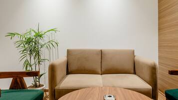 Uma sala de estar moderna com uma mesa de madeira redonda, um sofá bege e um banco estofado verde.