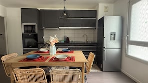 Une cuisine moderne avec des meubles de couleur sombre, un réfrigérateur en acier inoxydable et une table à manger dressée avec des assiettes et un vase.