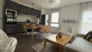 Une cuisine moderne avec des meubles de couleur sombre, un coin repas avec une table en bois et des chaises en osier, un canapé et une table basse.