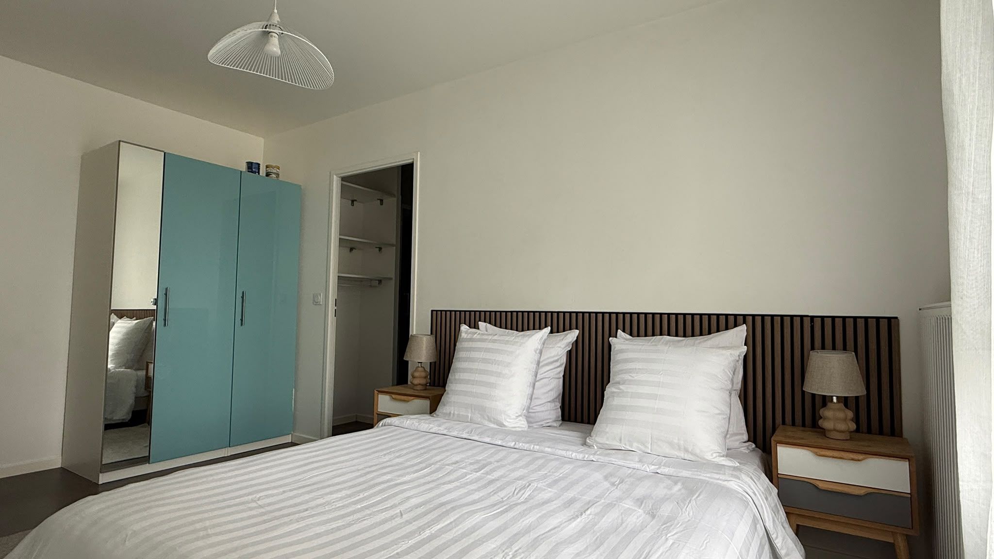 Une chambre à coucher comprenant un lit, deux tables de chevet, une commode, une armoire et un luminaire suspendu.