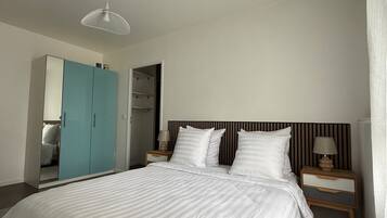 Une chambre à coucher comprenant un lit, deux tables de chevet, une commode, une armoire et un luminaire suspendu.