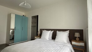 Une chambre à coucher comprenant un lit, deux tables de chevet, une commode, une armoire et un luminaire suspendu.