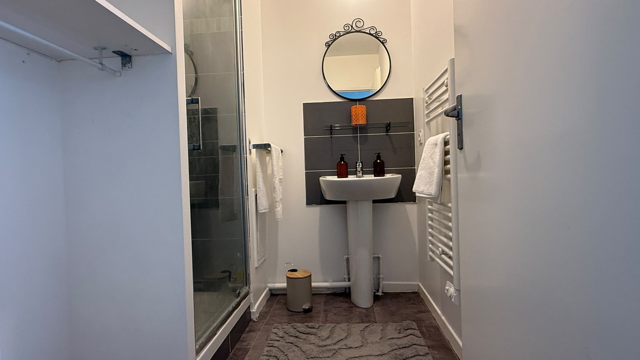 Une petite salle de bain dotée d’une douche à parois de verre, d’un lavabo sur colonne et d’un miroir placé au-dessus.