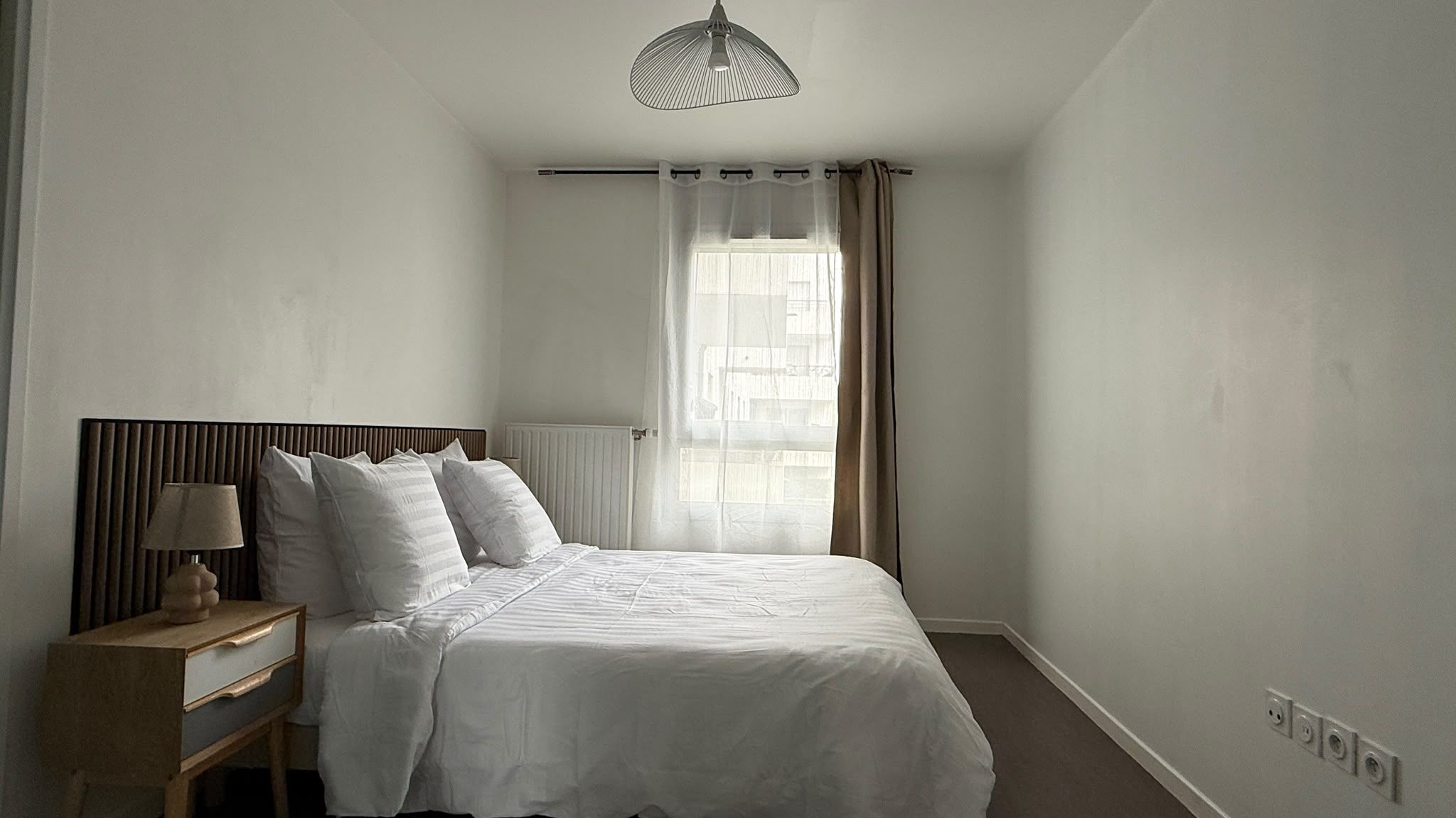 Une chambre à coucher avec un lit, une table de chevet, une lampe et une fenêtre avec des rideaux.