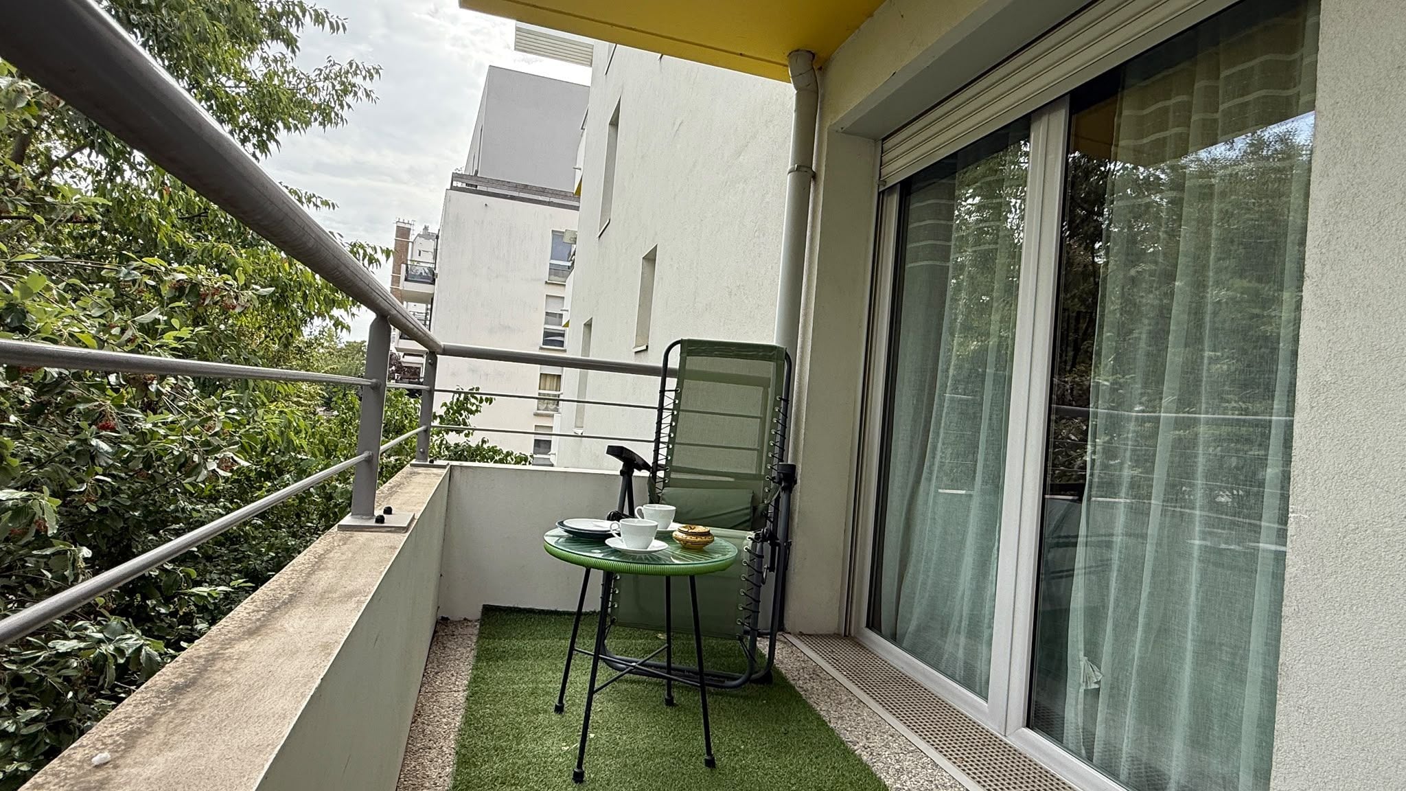 Un balcon avec une petite table, des chaises et une fenêtre avec des rideaux.