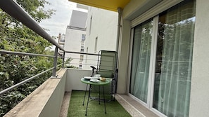 Un balcon avec une petite table, des chaises et une fenêtre avec des rideaux.
