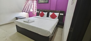 A bedroom with a bed, a nightstand, a window with curtains, and a wall with a sign. - Hotel Airport Shine Inn (Hyderabad)