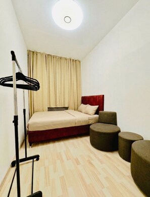 A compact bedroom with a bed, a standing lamp, a radiator, and a small seating area with ottomans. - Vienna Hideaway Private Room for Two (Wien)