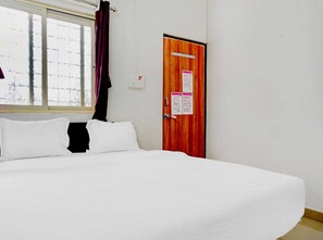 Ein Hotelzimmer mit Bett, Fenster mit Vorhängen, einer Holztür mit Aushängen und einer Steckdose.