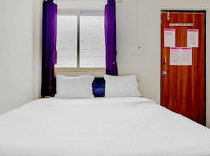 Ein Hotelzimmer mit einem Bett, einem Fenster mit violetten Vorhängen und einer Tür mit angebrachten Aushängen.