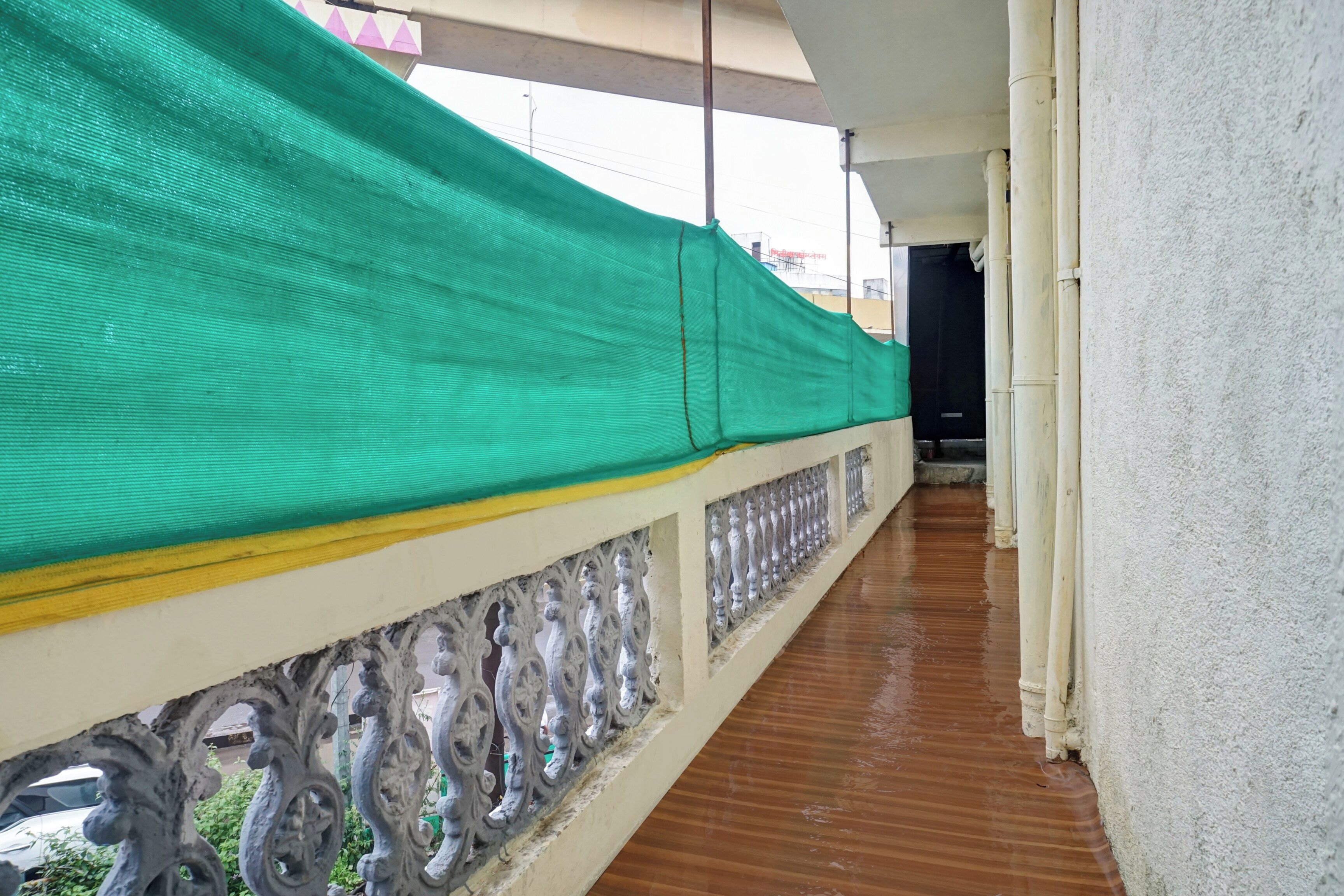 A covered balcony with a green protective cover, a wooden floor, and decorative balustrade.