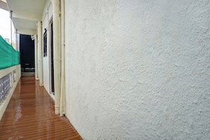A corridor with white walls and a wooden floor, leading to a door with a green tarp.