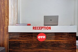 Un mostrador de recepción con una laptop y un libro, con la etiqueta 'RECEPTION' y 'OYO' respectivamente.