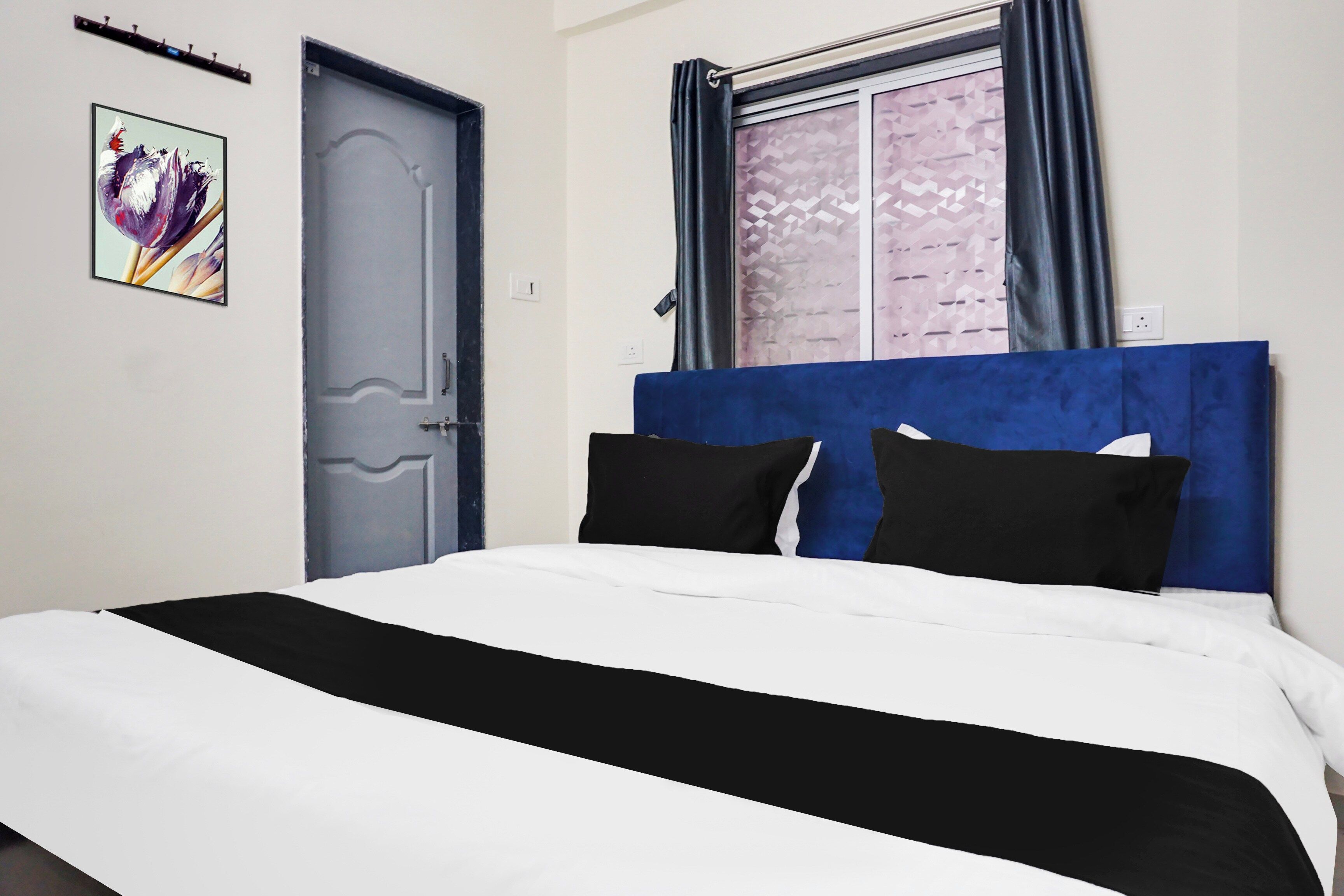 Un dormitorio con cama, una puerta, una ventana con cortinas y un cuadro colgado en la pared.