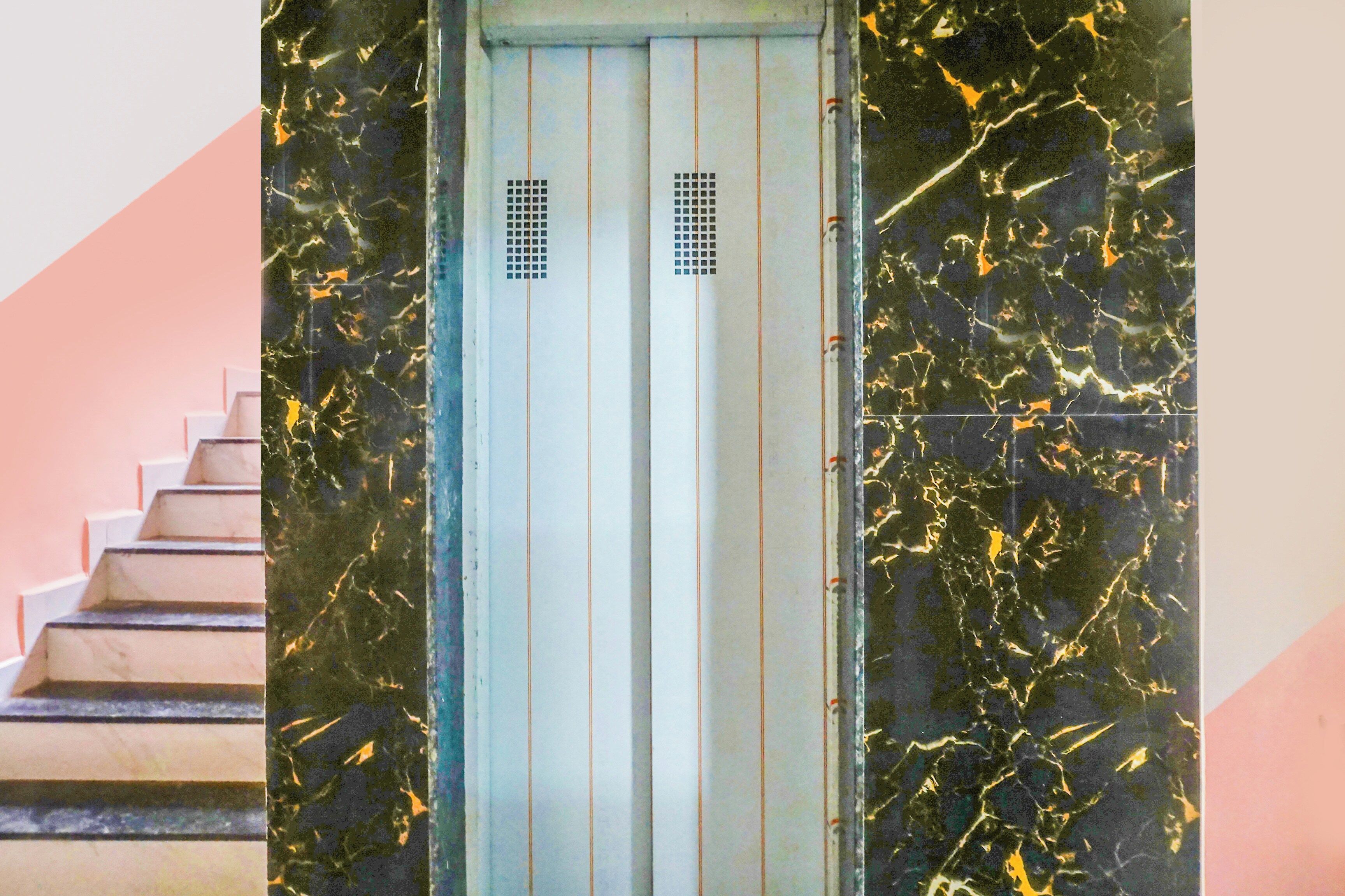 Una escalera que conduce a un ascensor con un muro de mármol.