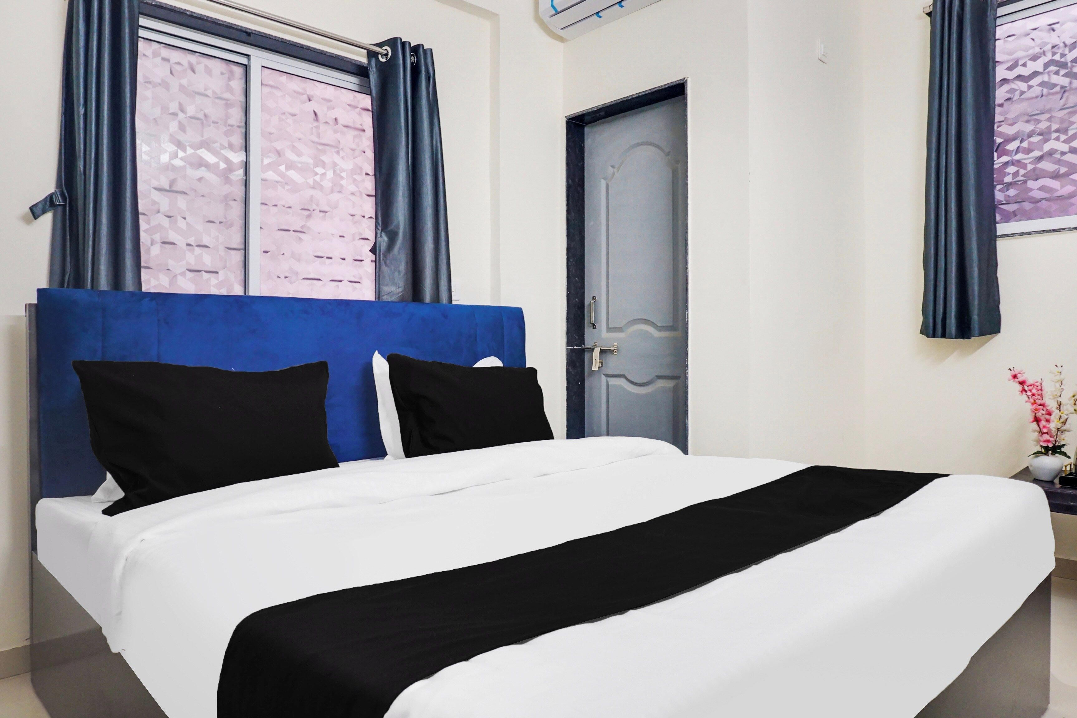 Una habitación de hotel con una cama, una puerta y un ventanal con cortinas.