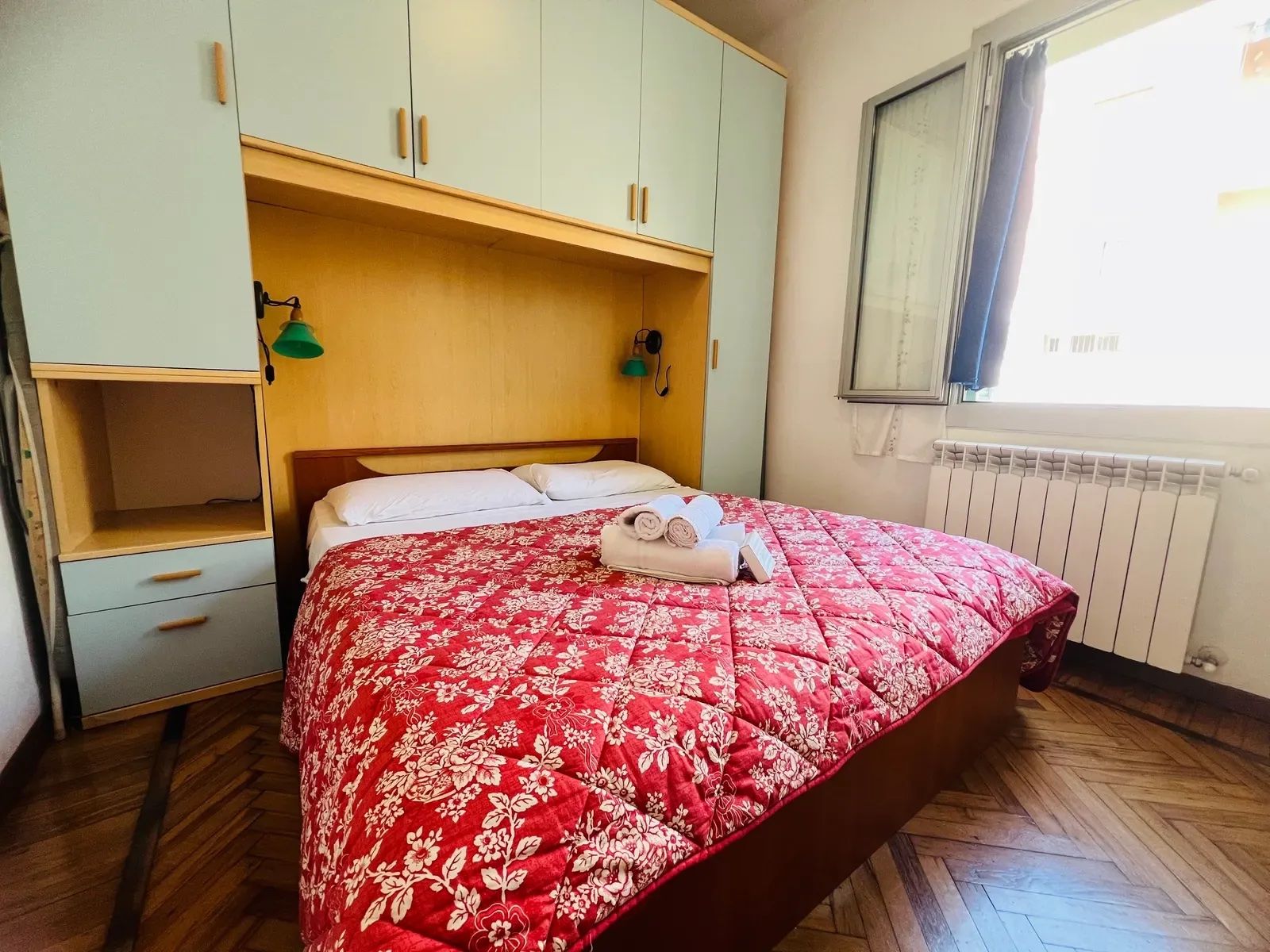 A bedroom with a bed, a wardrobe, a window, and a radiator.
