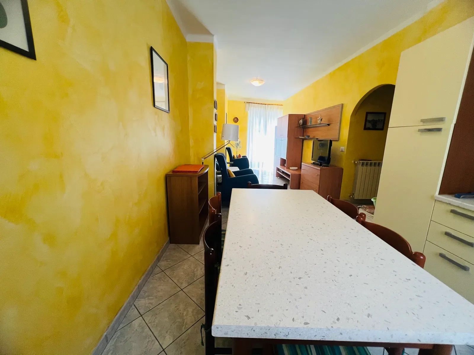 A dining area with a long table, chairs, and a kitchen area with cabinets and a stove.