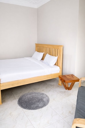 Uma cama de solteiro com cabeceira de madeira, uma pequena mesa de cabeceira de madeira, um tapete felpudo cinza e um sofá cinza.