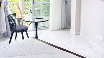 Une chambre d’hôtel avec un lit, une table ronde et une chaise, un balcon avec des rideaux et un téléviseur fixé au mur.