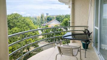 A balcony with a table and chair, a potted plant, and a view of greenery and buildings.