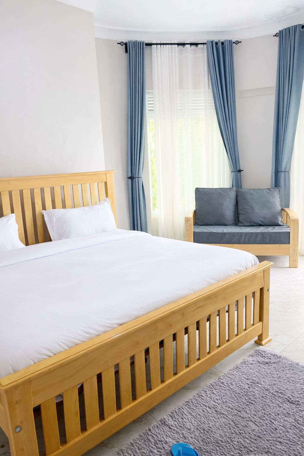 Une chambre à coucher avec un lit en bois, un canapé gris et des rideaux bleus.