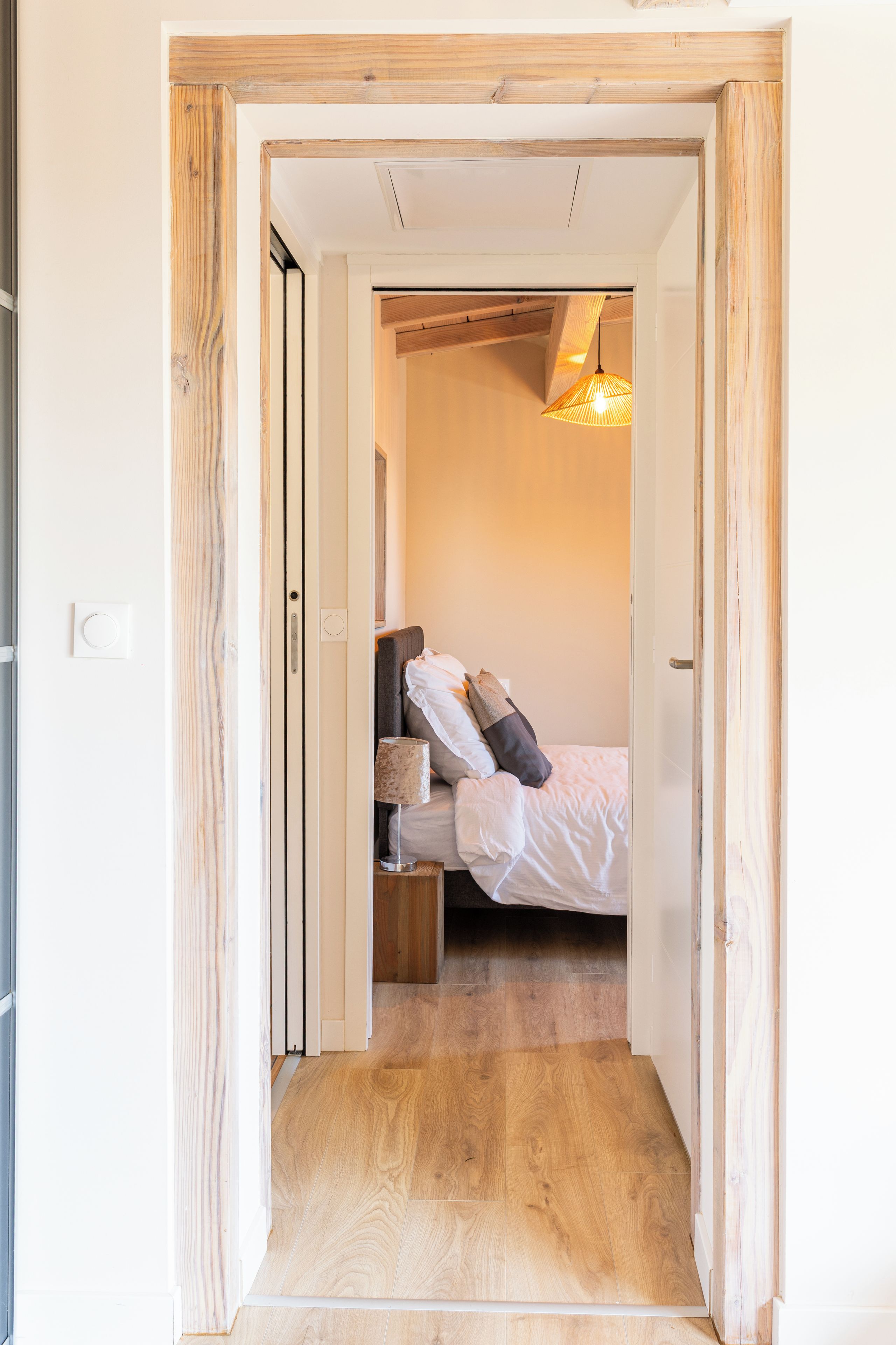 Un pasillo estrecho que conduce a un dormitorio con una cama, una mesita de noche y una lámpara.