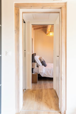 Un pasillo estrecho que conduce a un dormitorio con una cama, una mesita de noche y una lámpara.
