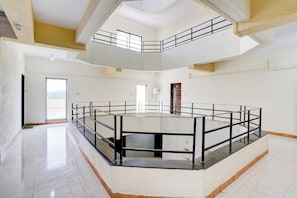 A spacious atrium with a central open area surrounded by a glass railing, high ceilings, and a view of the outdoors. - Hotel O Krupa Lodge (Paud)