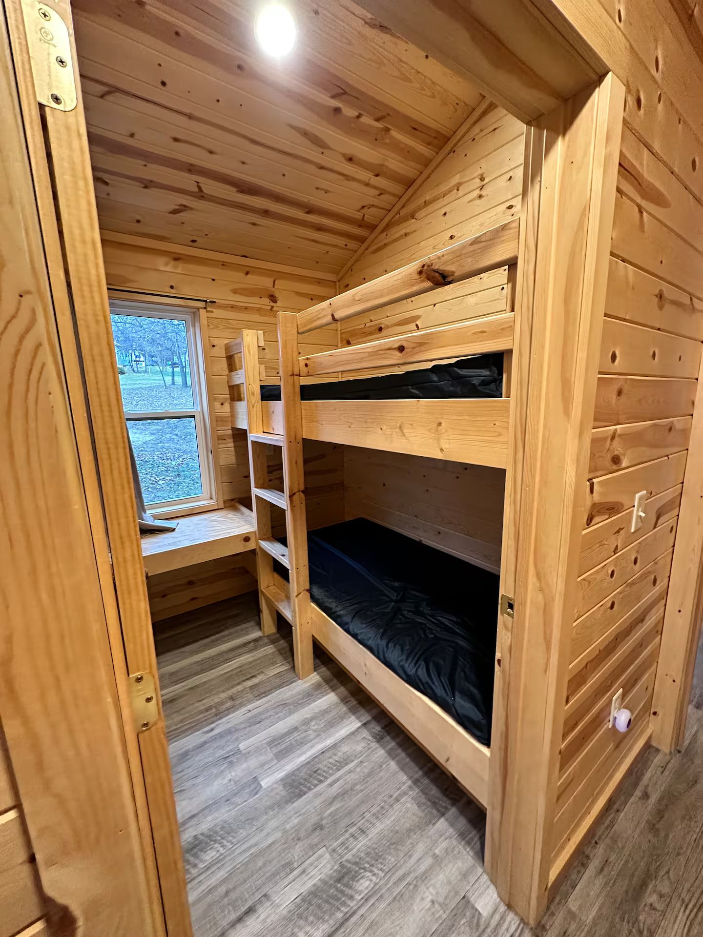 A wooden bunk bed room with a window, a shelf, and a door.