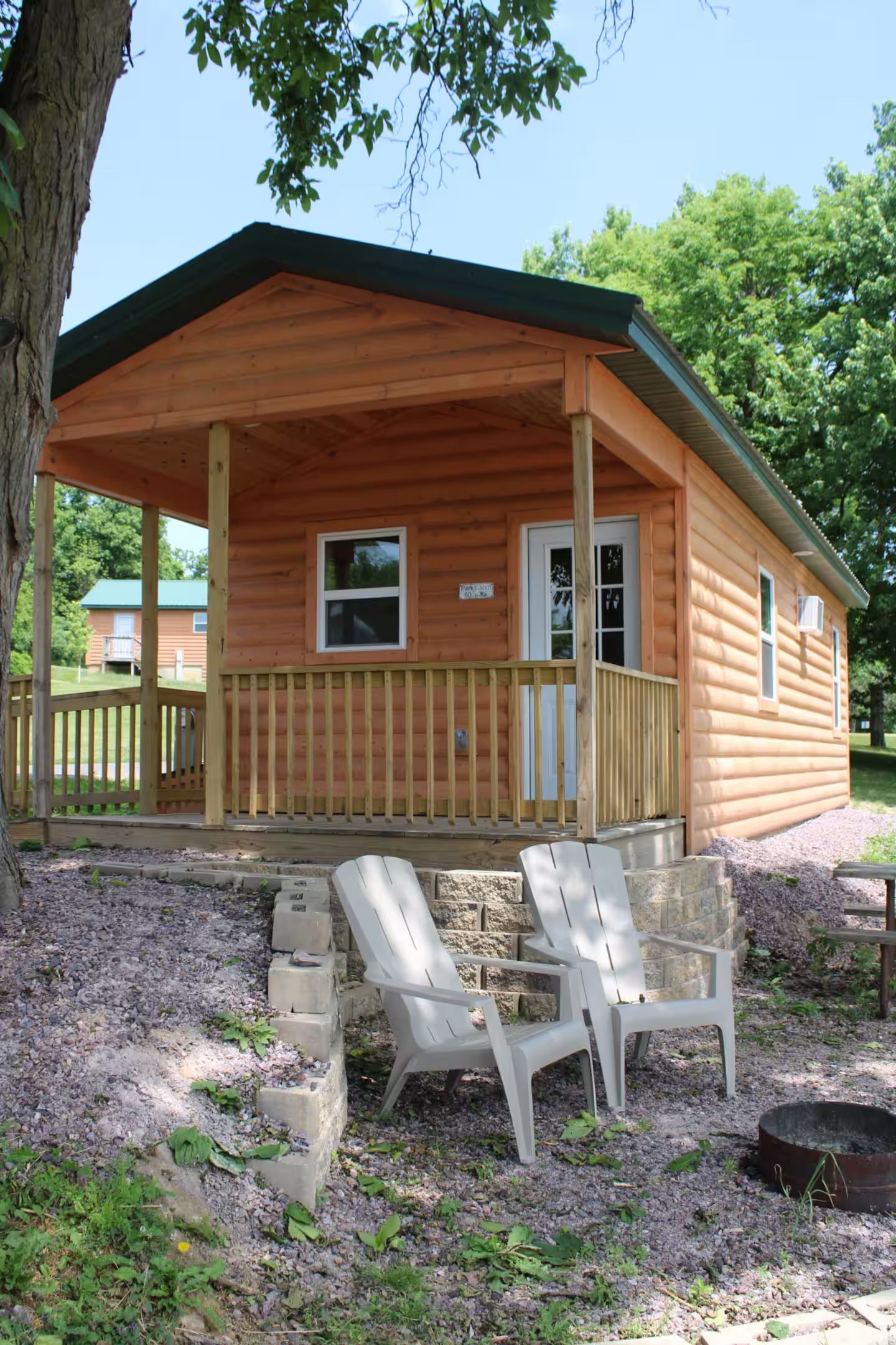 A wooden cabin with a porch, two Adirondack chairs, and a fire pit.