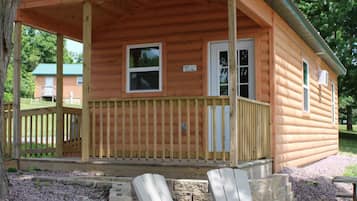 A wooden cabin with a porch, two Adirondack chairs, and a fire pit.