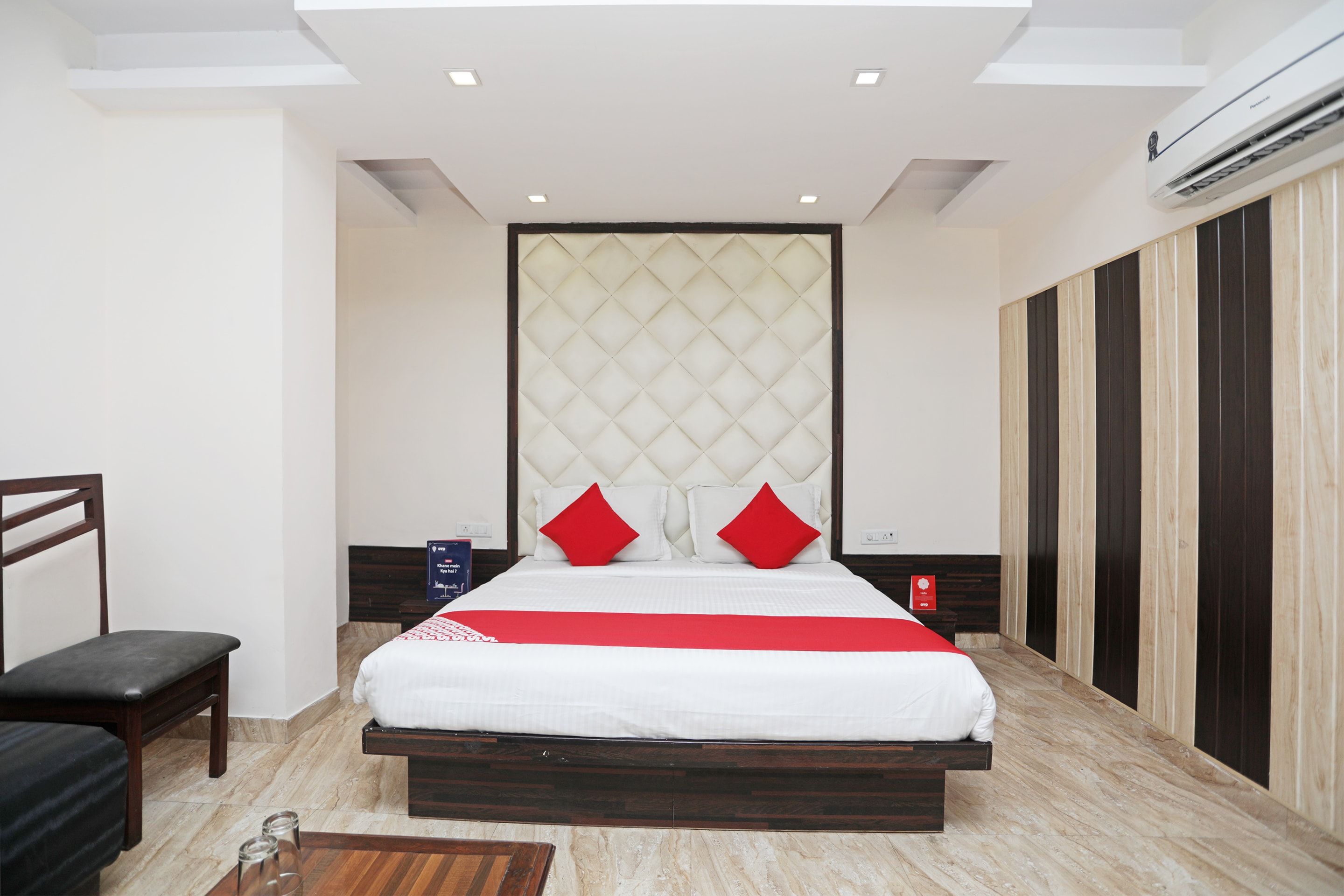 Una habitación de hotel moderna con una cama grande, un banco de madera, una mesita de noche y un armario.
