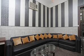 A modern lounge area with a black leather sofa, a glass coffee table, and a wall-mounted air conditioning unit. - Hotel O Subhadra Residency (Meerut)